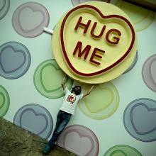 A man holding a giant love hearts sweet with the words hug me written on it.